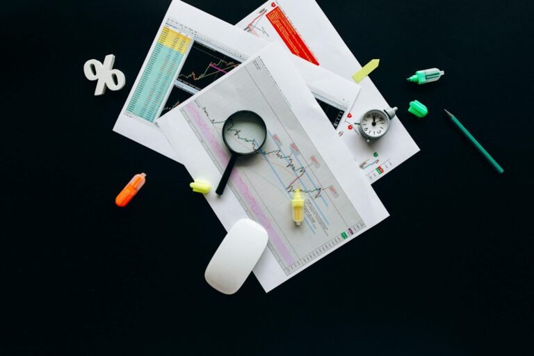 Overhead view of an office desk with financial documents, a magnifying glass, and stationery items, suggesting business analysis.